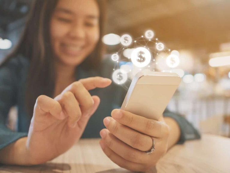 Imagem mostra uma mulher mexendo no seu celular e várias cifras aparecendo para ela, simulando, O que é o salário emocional