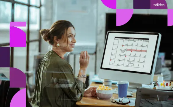 Mulher em um escritório olhando para a tela de um computador que exibe um calendário com datas marcadas, representando o planejamento de feriados e pontos facultativos.