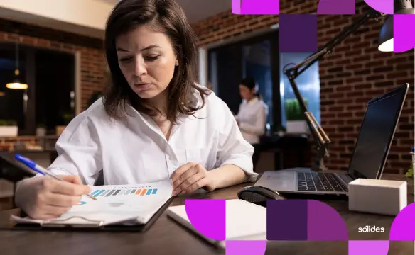 Gestora financeira analisando relatórios de custos e gráficos para decidir entre banco de horas ou horas extras.