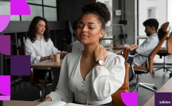 Mulher jovem em ambiente de escritório, sentada à mesa com os olhos fechados e a mão no pescoço, expressando cansaço mental ou estresse. Ao fundo, colegas de trabalho e elementos gráficos da Sólides