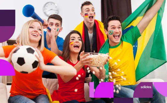 Grupo de jovens profissionais com camisas e bandeiras de diferentes países comemorando e assistindo a um jogo, ilustrando o horário de trabalho na Copa do Mundo. No canto inferior direito, o logotipo da Sólides sobreposto a elementos gráficos roxos.