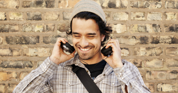 homem sorrindo colocando os fones de ouvido, ele usa touca e tem barba, representando a Geração Y