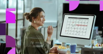 Mulher em um escritório olhando para a tela de um computador que exibe um calendário com datas marcadas, representando o planejamento de feriados e pontos facultativos.