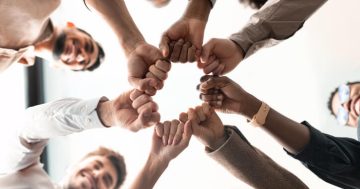 pessoas lado a lado em roda, unindo seus punhos fechados ao centro, representando equipes engajadas