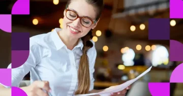 Mulher sorridente com óculos analisando relatórios manuais, representando a importância de monitorar os KPIs de Folha de Pagamento para garantir a saúde financeira da empresa com o Software de RH da Sólides.