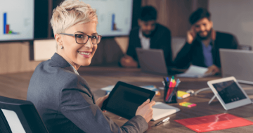 pessoa de roupa social em ambiente corporativo com dispositivo móvel nas mãos sorrindo demonstrando satisfação no trabalho