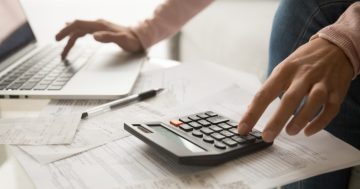 calculo de custo do funcionario, imagem mostra uma pessoa usando o notebook e calculadora ao mesmo tempo.