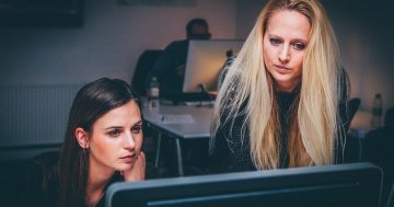 Duas mulheres olhando para o computador, simulando que estão calculando folha de pagamento online