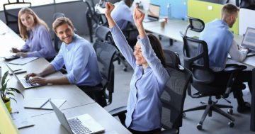 pessoa em escritório fazendo gesto comemorativo em meio a demais colegas simulando competitividade no trabalho