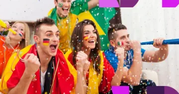 Colaboradores diversos com pinturas no rosto e bandeiras, celebrando com confetes e cornetas, ilustrando o engajamento de equipes durante a Copa do Mundo.
