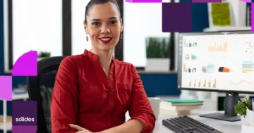 Mulher sorridente no escritório analisando dados em um monitor, ilustrando como a integração entre Controle de Ponto e Folha de Pagamento elimina erros e atrasos no Departamento Pessoal da Sólides.