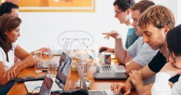 diversas pessoas sentadas juntas em uma mesa trabalhando em seus notebooks