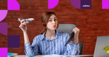 Colaboradora sorridente sentada em sua mesa de escritório na Sólides, segurando uma miniatura de avião em uma mão e um tablet na outra, simbolizando o retorno das férias ao trabalho com um notebook aberto à sua frente.