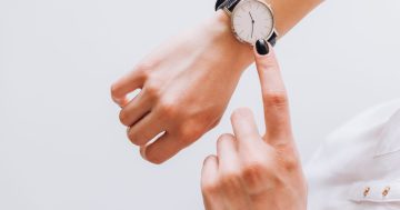 foto de um relógio em um pulso e um dedo feminino apontando para e ele representando atrasos no trabalho